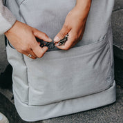 Grauer Rucksack mit Schlüsselkarabiner im Frontfach.  Fair produziert von Anna und Oskar